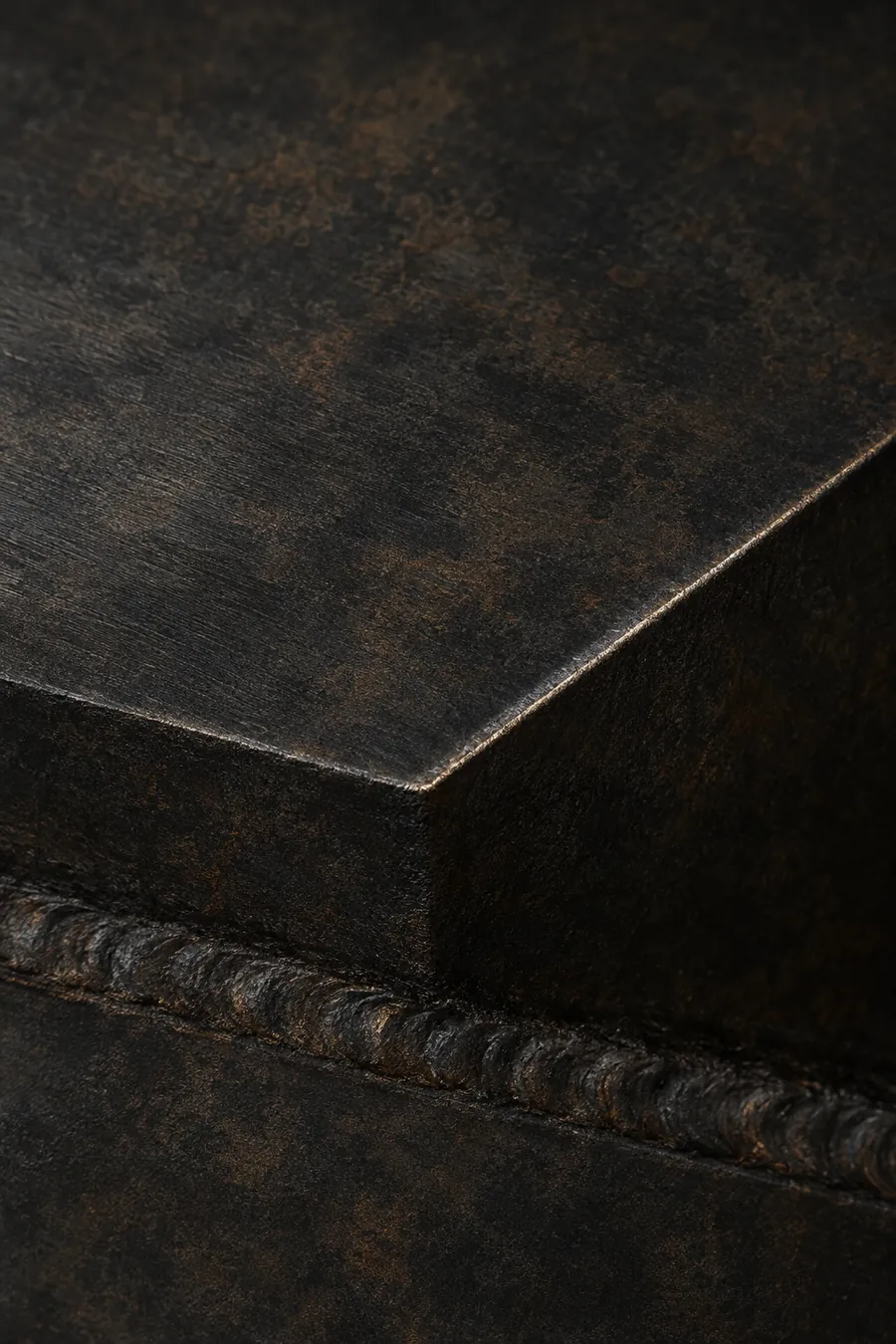 Close-up of hand-blackened mild steel showing a weld bead and chamfered edge